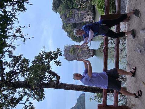       Two travellers posing playfully with the iconic limestone islet known as James Bond Island in the background.
  