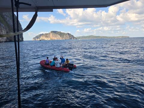      Inflatable red dinghy carrying tourists across deep blue waters with limestone islands of Phi Phi in the distance.
  