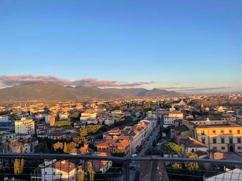       Wide cityscape of Pisa with distant mountains under warm late-day light
  