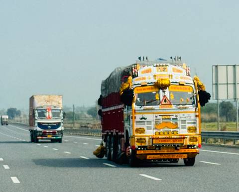       Colorfully painted Indian freight trucks driving along a highway.
  