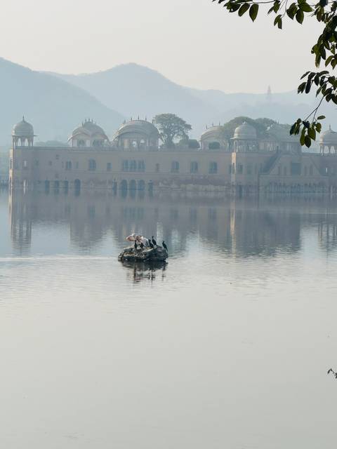       Misty morning view of Jal Mahal floating palace reflected on a calm lake.
  