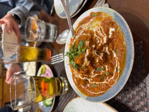       Close-up of rich curry garnished with cream and herbs at a restaurant table.
  