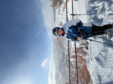       Smiling hiker with trekking poles overlooks the snow-filled amphitheater of Bryce Canyon under sparkling skies.
  