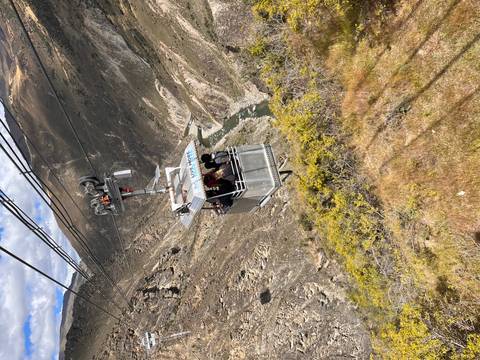       Open cable car suspended over a deep river canyon carrying thrill-seekers.
  