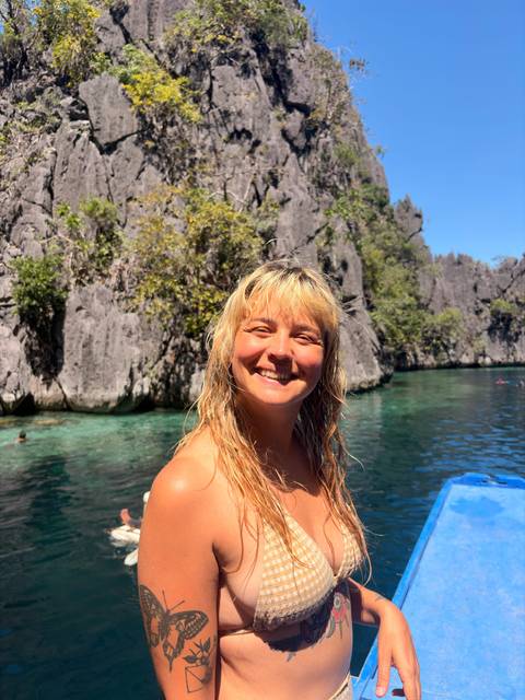       Young woman smiling on a boat in a turquoise lagoon surrounded by dramatic limestone cliffs
  