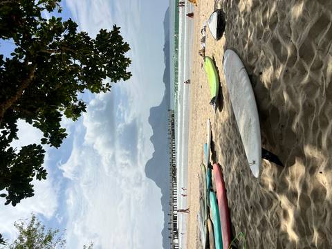       Sandy beach with several surfboards, gentle waves, distant limestone cliffs and a pier under partly cloudy skies
  