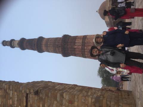       Elderly travellers stand before the soaring Qutub Minar while other visitors mill around.
  