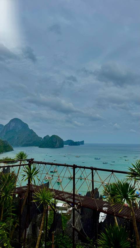       Cloudy seascape of dramatic limestone islands and turquoise bay waters dotted with boats.
  