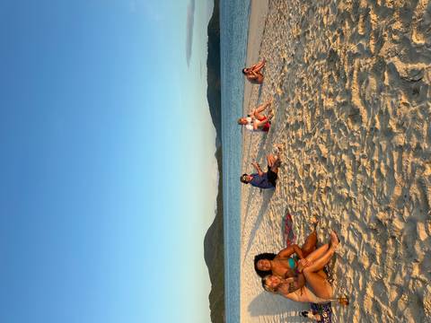       Group of friends lounge and chat on a wide sandy beach in late afternoon light.
  