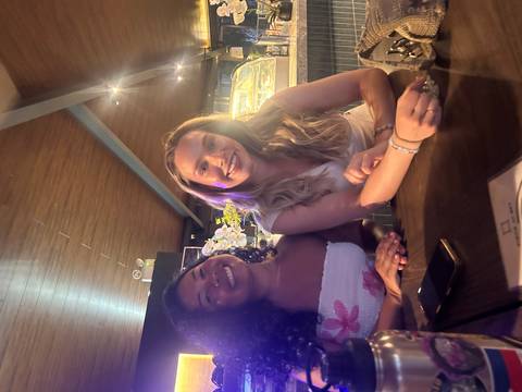       Two young women smiling at a bar-style table inside a cozy restaurant
  