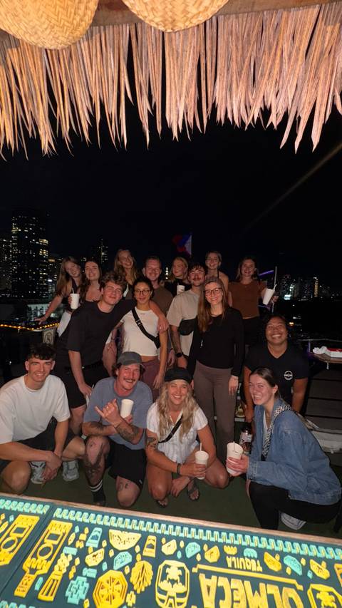       Large group of travelers posing together on a rooftop at night with city lights behind
  