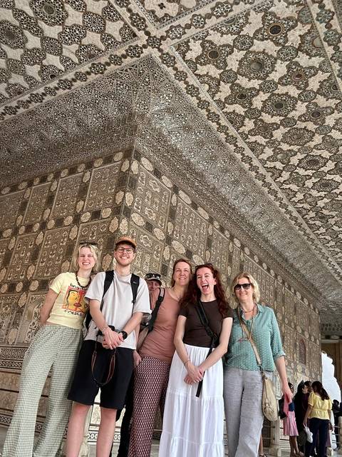       Smiling travel group posing inside a richly decorated hall lined with mirrored mosaic and carved stone.
  