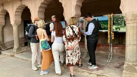       Tour guide explaining historical panels to a small tour group in an arched stone pavilion.
  