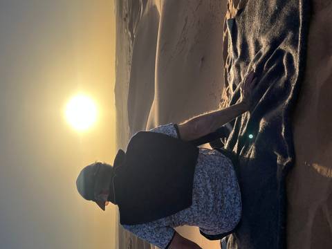       Traveller seated on a blanket watching the sun set over rolling Sahara dunes.
  