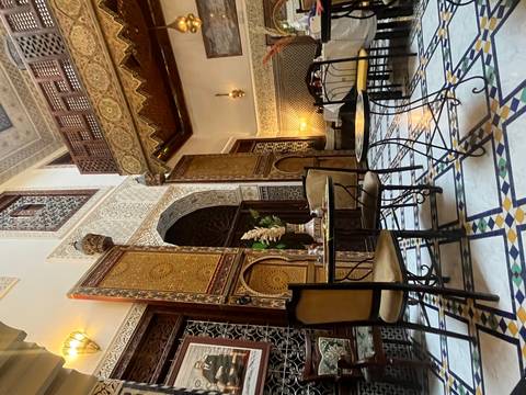       Lavishly decorated riad dining area with mosaic floor, carved plaster walls and wooden balcony.
  