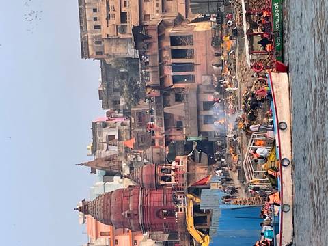       Busy riverbank ghats of Varanasi with cremation fires burning and colourful temples rising behind.
  