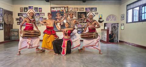       Traditional Sri Lankan dancers in colorful costume performing indoors.
  