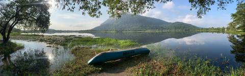       A lone canoe rests on the edge of a calm lake reflecting a green mountain.
  