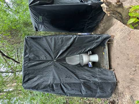       Makeshift outdoor toilet inside a black plastic tent.
  