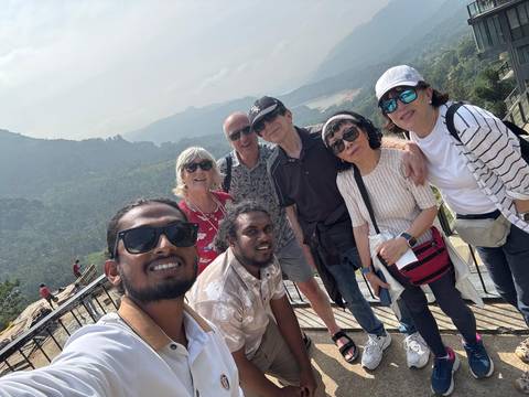       Energetic group selfie on a mountain walkway with forested hills behind.
  
