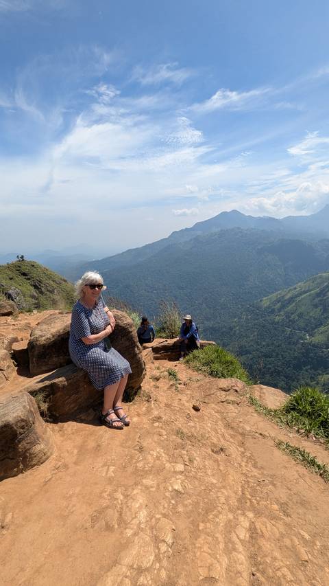       Woman resting on rocks above a sweeping mountain panorama as companions relax nearby.
  