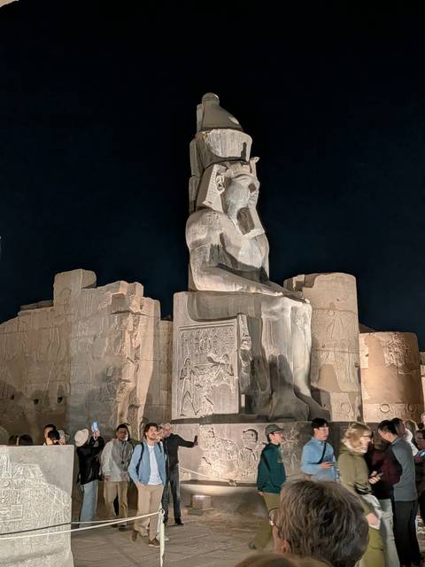       Illuminated colossal statue of Ramses II at Luxor Temple captured against the night sky.
  
