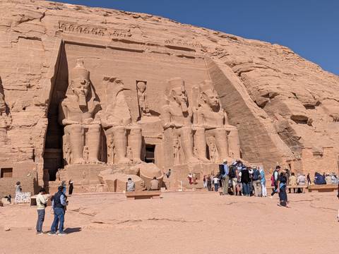       Front façade of Abu Simbel with massive statues of Ramses II and crowds of visitors at its base.
  