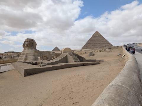      Wide angle of the Sphinx and the Great Pyramid under a partly cloudy sky on the Giza plateau.
  