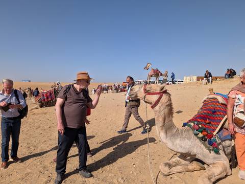       Busy scene of travellers and camel handlers on the sandy desert near the pyramids.
  