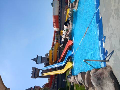       Colourful water slides plunging into a bright blue hotel pool at an outdoor aqua park.
  