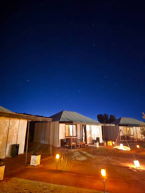       Clear starry night sky above simple desert camp tents glowing faintly.
  