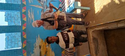       Visitor holding a baby crocodile beside a local boy inside a brightly painted Nubian home.
  