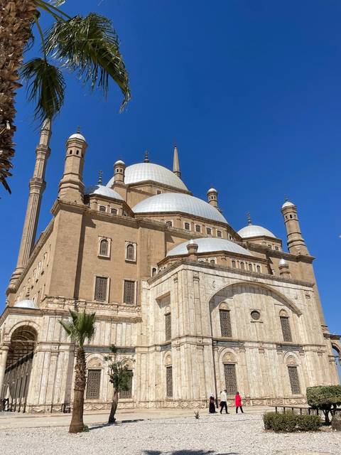       The sandstone Mohammed Ali Mosque with soaring minarets and white domes under a clear blue Cairo sky.
  