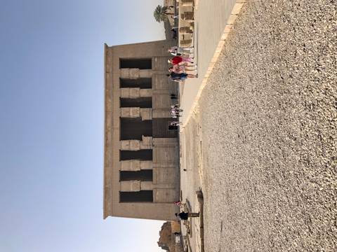       Visitors approach a massive stone facade of an ancient Egyptian temple on a bright sunny day.
  