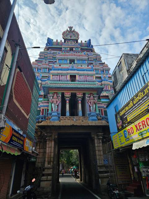       Street-level view of a colourful South Indian temple entrance nestled between urban buildings.
  