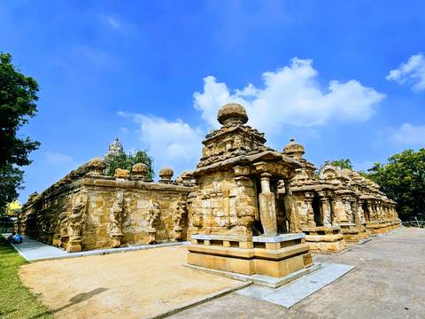       Brightly lit ancient stone temple complex with carved pillars under a vivid blue sky.
  