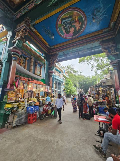       Bustling temple market arcade filled with colourful stalls, visitors and religious décor.
  