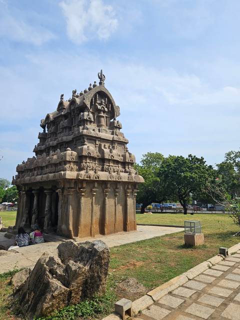       Stone monolithic shrine of the Pancha Rathas complex set against grass and trees.
  