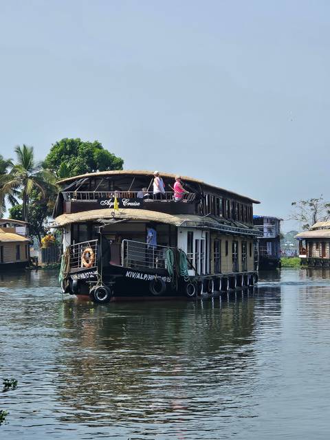       Traditional Kerala houseboat cruising the backwaters with two passengers on the upper deck.
  