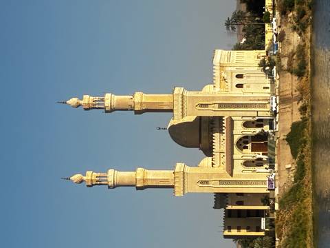       Elegant twin-minaret riverside mosque glowing golden in late afternoon light.
  