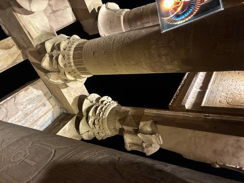       Night-lit hieroglyphic columns of an ancient Egyptian temple captured dramatically against black sky.
  