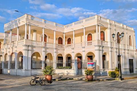       Cream-colored neoclassical building with arched balconies and blue sky backdrop.
  