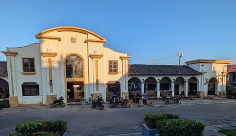       Long, low colonial building with arched portico and motorbikes parked out front in evening light.
  