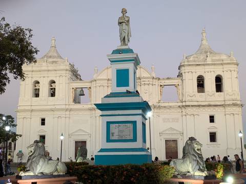       Front plaza of León Cathedral with turquoise monument base and white twin-towered church at dusk.
  