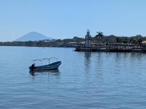       Small motorboat on a calm lake with lighthouse pier and a cone volcano in the distance.
  
