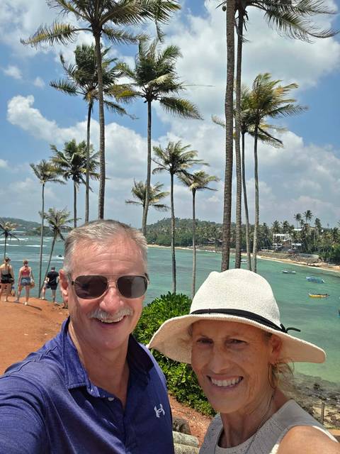       Visitors posing on a palm-fringed headland overlooking turquoise ocean waves.
  