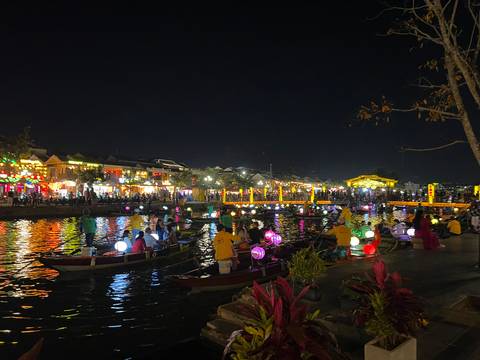      Nighttime scene of colorful lantern-lit boats and bustling riverside in Hoi An.
  