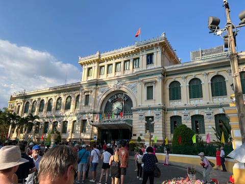       Colonial-era Saigon Central Post Office with crowds of visitors in front under late-day light.
  
