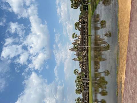       Iconic Angkor Wat temple reflected in still moat under partly cloudy skies.
  