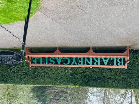       Wooden bench with large green letters spelling 'BLARNEY CASTLE' set against tall manicured hedges.
  